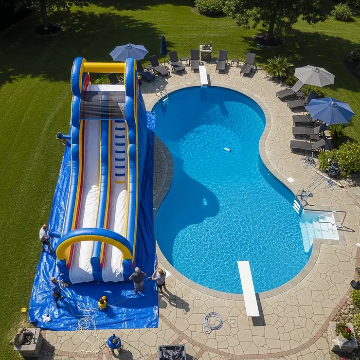 An aerial view of an inflatable pool slide being set up next to a large in-ground pool.