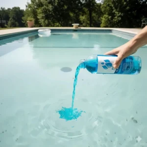 A hand pouring liquid clarifier into a swimming pool near a return jet to properly disperse the product and treat the water.