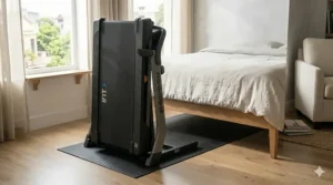 A compact treadmill folded vertically and standing against a wall in a small home office.