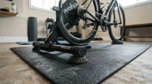 Close-up of a noise reduction bike mat absorbing vibrations beneath stationary trainer feet in a basement.
